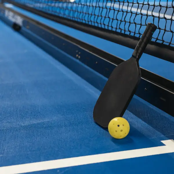 A pickleball paddle next to a ball laid on a pickleball court