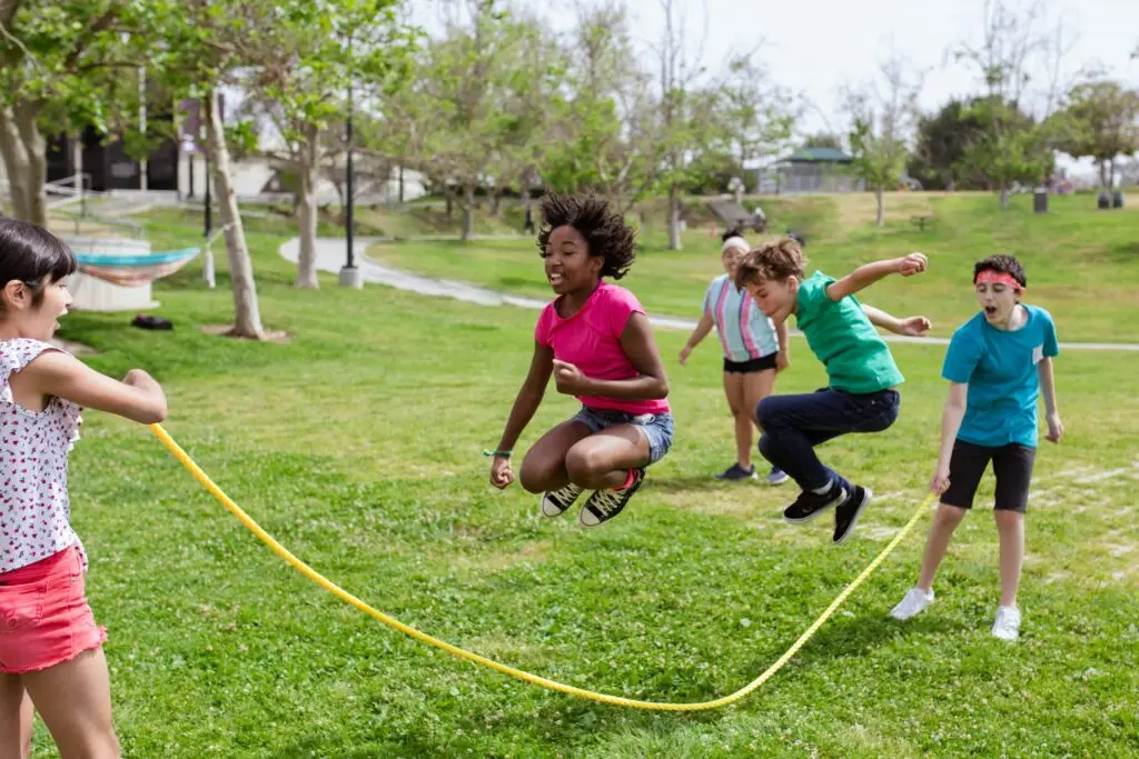 Kids playing with a jump rope on the grass.